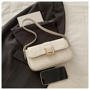 Close-up of white crocodile pattern shoulder bag with gold metal clasp on a black blazer