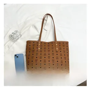 Detail view of brown tote bag with bear pattern and gold rivets next to a smartphone