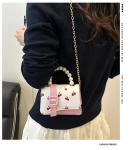 Detail of white cherry print mini bag with pink flap and pearl handle on navy blue sweater
