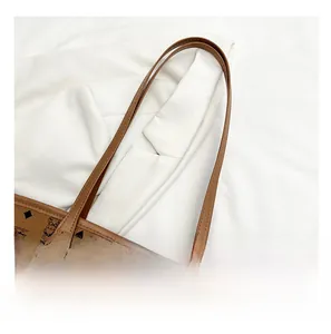 Detail of bear monogram tote bag with brown straps and golden rivets on white suit