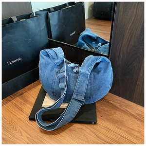 Detailed view of casual denim crescent bag with adjustable strap on wooden floor