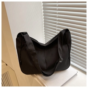 Detail of minimalist black nylon hobo tote bag featuring a wide strap on white books