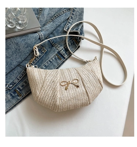 Detail of cream woven crossbody bag with gold bow ornament and textured finish