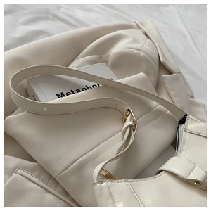 Vue de dessus d'un sac hobo demi-lune beige avec boucles dorées sur un blazer couleur ivoire
