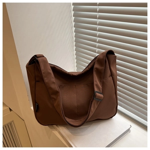 Detail of dark brown nylon crossbody bag featuring an adjustable wide strap and side label
