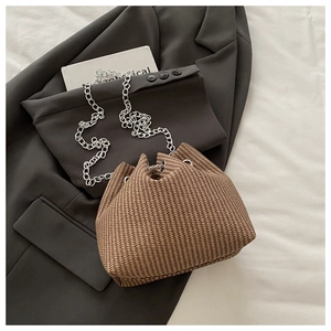 Détail d'un sac seau tissé marron avec chaîne argentée posé sur une veste grise