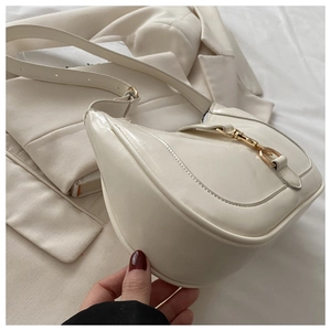 Détail du sac demi-lune blanc avec boucle à piston dorée posé sur une veste chic