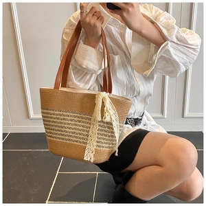Detail of straw woven tote with brown leather handles and decorative lace ribbon