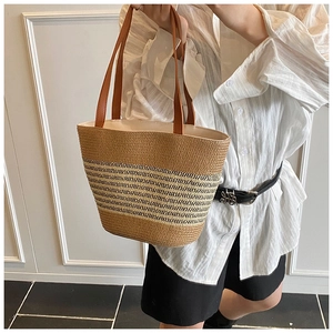 Detail of hand-woven straw tote with black stripes and brown leather handles