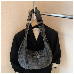 Detail of washed black denim hobo bag featuring a front pocket and vintage distressed finish