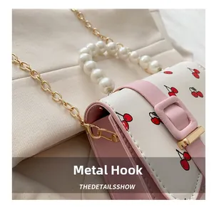 Detail of gold metal hook and cherry print on white and pink crossbody handbag
