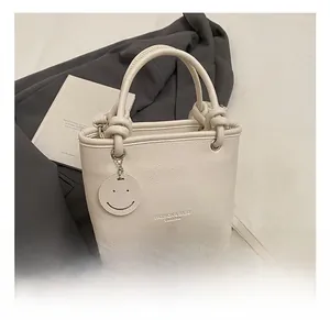 Detail of white lychee leather bucket bag with knotted handle and smiley face charm