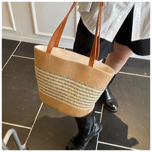 Detail of striped straw woven tote bag featuring brown leather straps for summer vacation