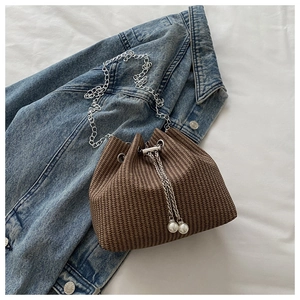 Détail du sac seau marron tressé avec chaîne argentée et cordons à perles blanches