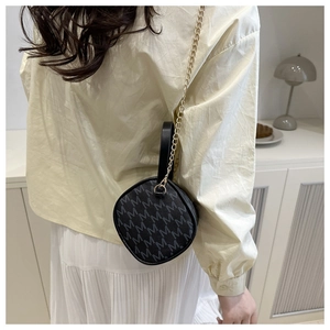 Detail of round black handbag with M print, golden chain strap, and leather top handle