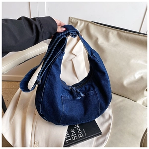 Detail of dark blue denim hobo bag with outer pocket and fringe zipper pull detail