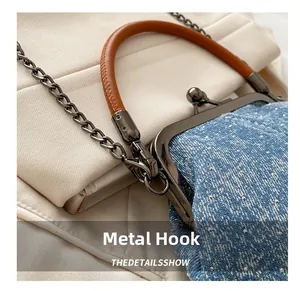 Detailed macro view of gunmetal snap hooks and brown leather handle on a denim bag