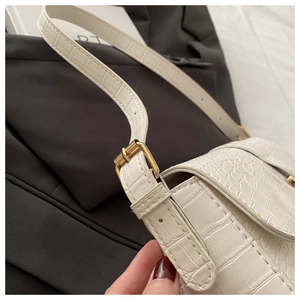 Detail of white crocodile embossed PU leather handbag with adjustable gold buckle strap