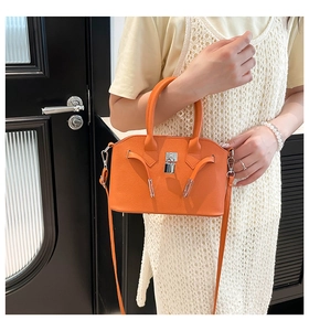 Detailoverzicht van feloranje kiezellederen handtas met iconisch zilveren hardware