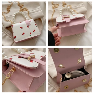 Detail of pink cherry print small square bag featuring pearl handle and gold chain strap