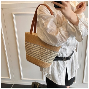 Detail of hand-woven straw tote bag with black stripes and brown leather straps