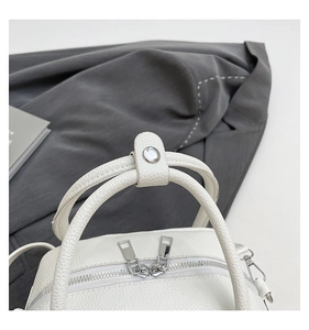 Close-up of white lychee pattern leather handbag with silver zippers and snap handle