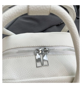 Detailed macro view of dual silver metal zippers on white lychee textured leather handbag