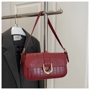 Detail of dark red croc-embossed leather shoulder bag with bold gold U-shaped buckle