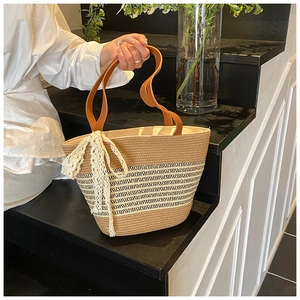 Detail of woven straw tote bag featuring white lace ribbons and brown leather handles