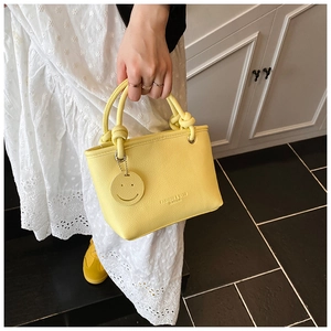 Detail of yellow lychee pattern PU leather handbag with knot handle and smiley charm