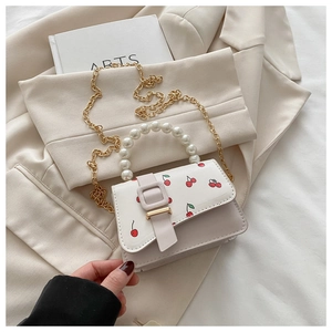 Detail of a chic cream crossbody bag with cherry prints, pearl handle and gold chain strap