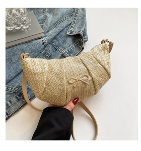 Close-up of woven beige crescent bag featuring a delicate gold bow accent and zip detail