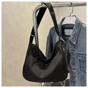 Detail of a black canvas crescent crossbody bag hanging next to a denim jacket