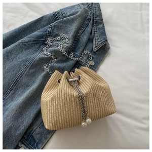 Détail du sac seau tressé beige avec cordon en chaîne argentée et ornements en perles