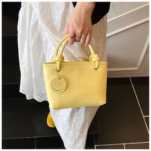 Detail of lychee pattern handbag featuring unique knot handle and yellow smiley charm