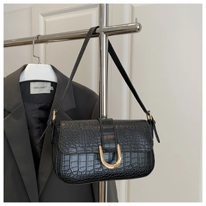 Close-up of black crocodile embossed leather shoulder bag with gold horseshoe buckle