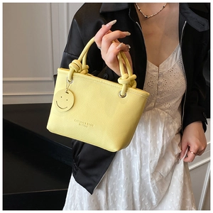 Close-up of bright yellow lychee grain tote bag with knotted handle and smiley pendant