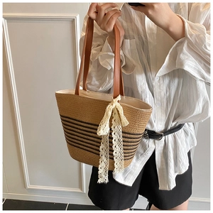 Detail of straw tote bag featuring white lace bow and black horizontal stripes