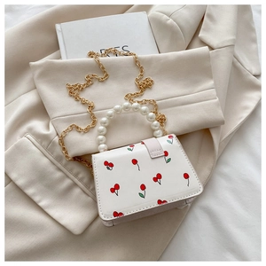 Detail of a mini white square bag with cherry prints, pearl handle and gold chain strap