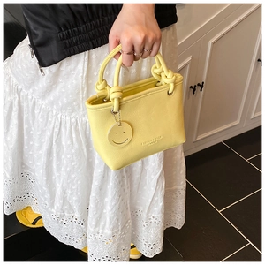 Macro view of bright yellow PU leather handbag with twisted knot handle and smile pendant