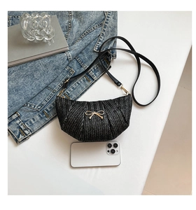 Detail of woven black mini crossbody bag with gold bow clasp and phone for size comparison