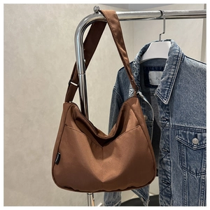 Detail of dark brown canvas crossbody bag featuring adjustable strap and woven side label
