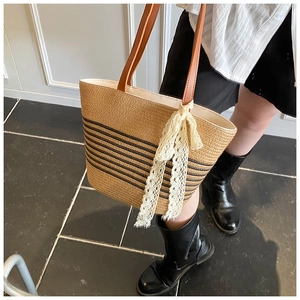 Detail view of woven straw tote bag with black stripes and elegant lace decorative ribbon