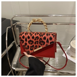 Detail of red crossbody bag with leopard print flap and golden braided metal handle