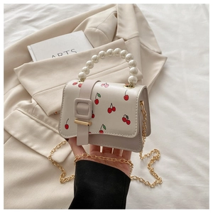 Macro shot of a cream mini bag with cherry print, pearl handle and gold chain strap