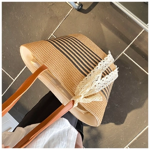Detail of straw tote bag with black stripes, leather handles, and a lace bow charm