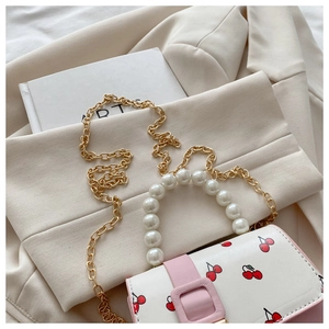 Detail of cherry print handbag with pearl handle and golden chain strap on beige background