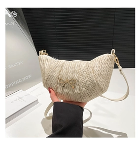 Close-up of woven crescent bag featuring a metallic gold bow and slim leather strap