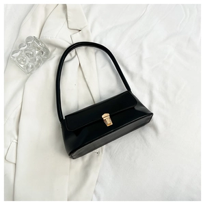 Detail of minimalist black baguette bag with gold metal buckle on white suit jacket