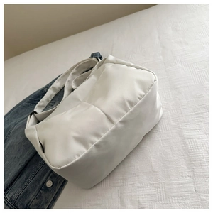 Detail of white quilted nylon shoulder bag with wide strap on a soft textured bedding